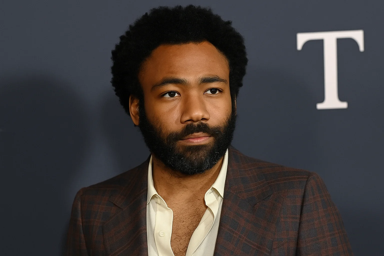 Donald Glover in a dark plaid suit and cream shirt, looking composed against a dark backdrop.
