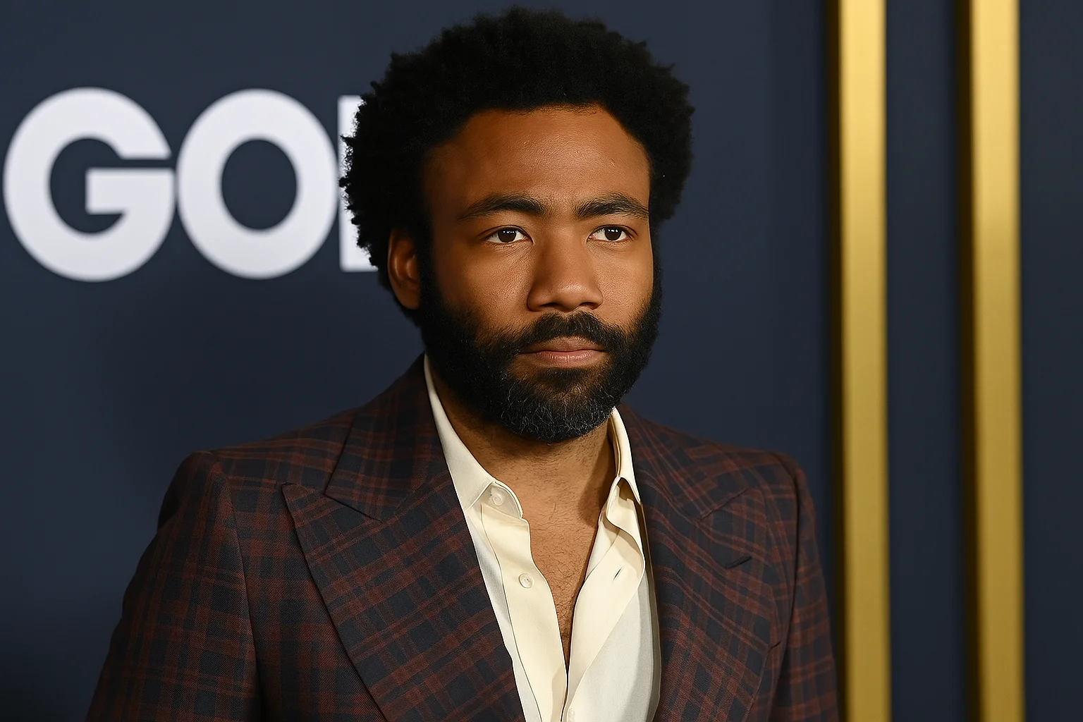 Donald Glover wearing a plaid suit jacket and cream shirt, posing confidently at a formal event.